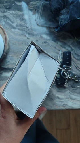 Hand holding a small white box on a marble surface with keys in the background