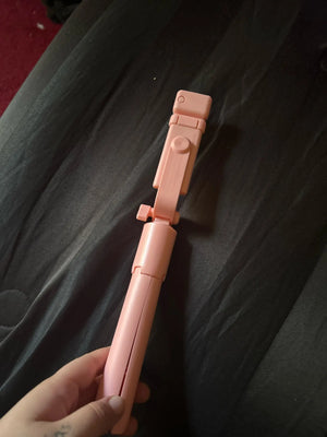 Pink selfie stick held by a hand on a dark fabric background