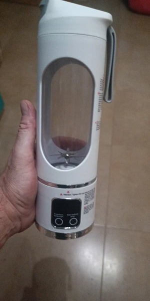 Hand holding a portable blender with a clear container on a light-colored floor.