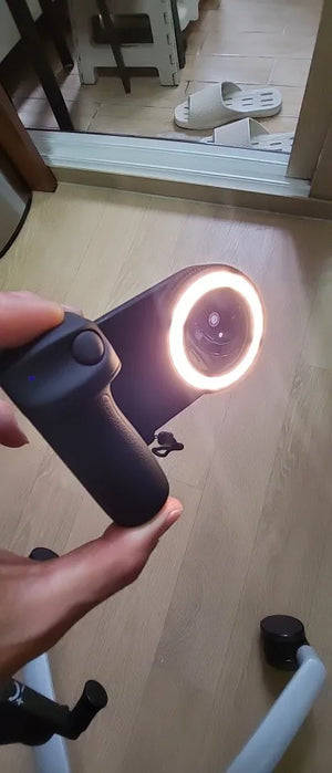 Hand holding a smartphone with a ring light in a room setting.