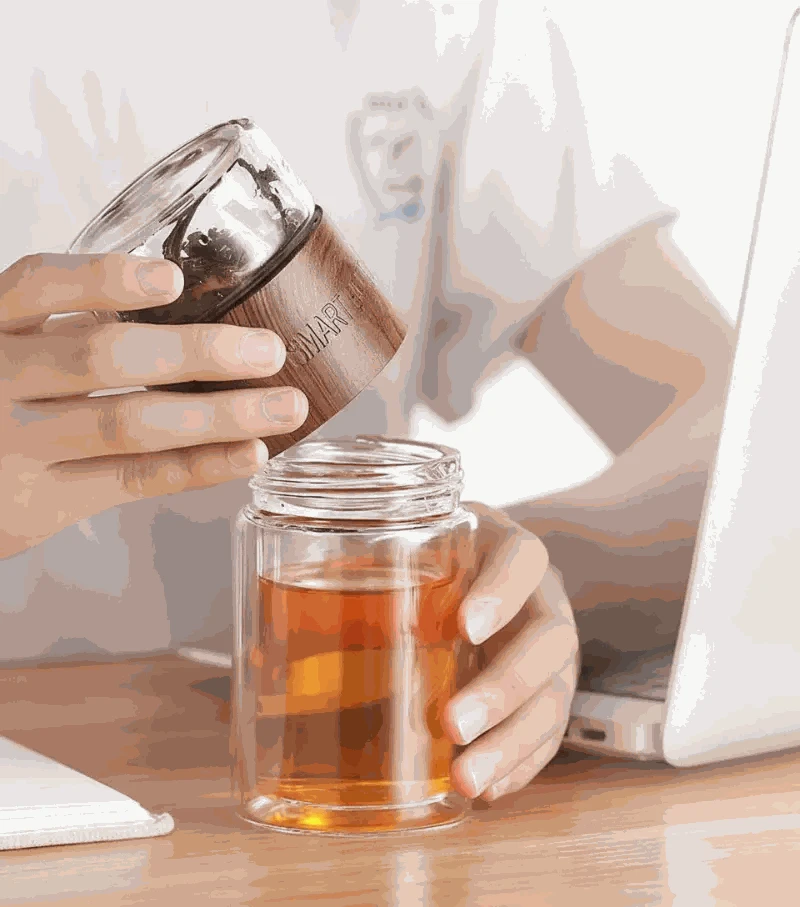Person holding a glass jar with tea and a smaller container, sitting at a desk.