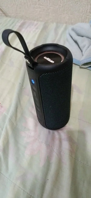 Black portable speaker on a bed with a white wall background