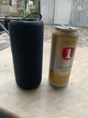 Black portable speaker next to a can of beer on a table