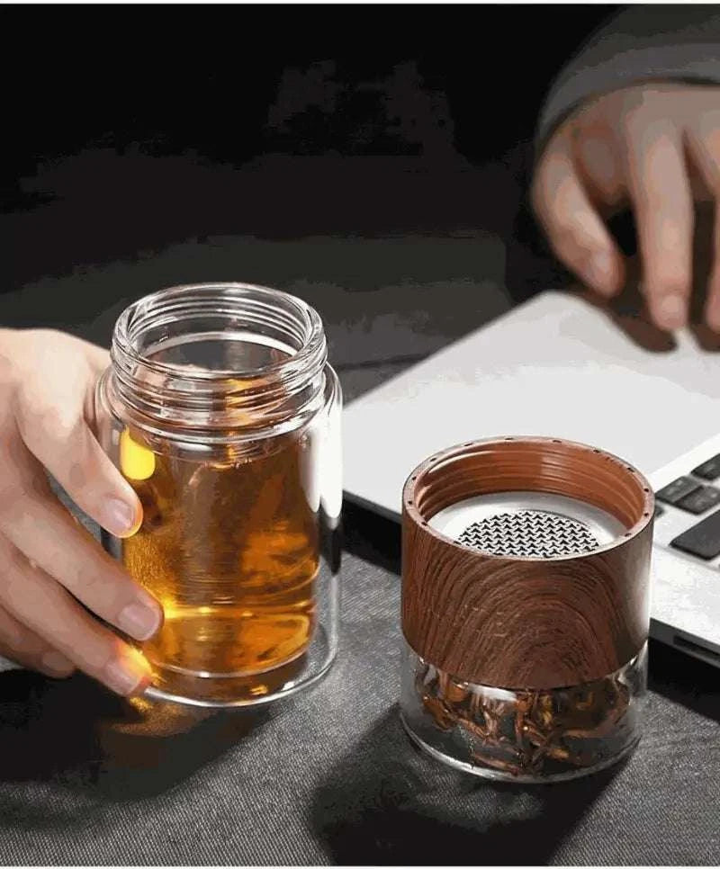 Two glass cups, one with a wooden sleeve, on a dark surface with a blurred background.