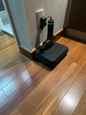 Black electronic device on a wooden floor with a wall outlet in the background