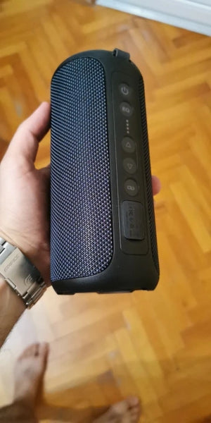 Hand holding a black portable speaker on a wooden floor