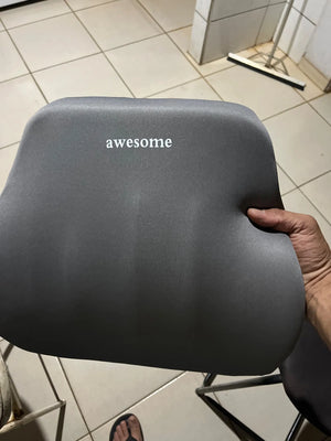 Gray cushion with 'awesome' text held by a person on a tiled floor.