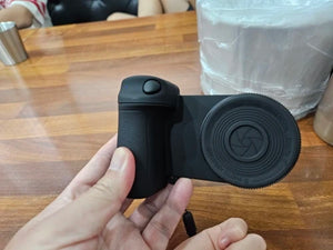 Black camera lens cap held by a hand on a wooden table