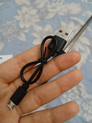 Hand holding a USB cable with micro USB connector against a floral-patterned background