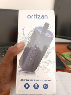  ortizan X8 Pro wireless speaker box held by a hand with a laptop in the background