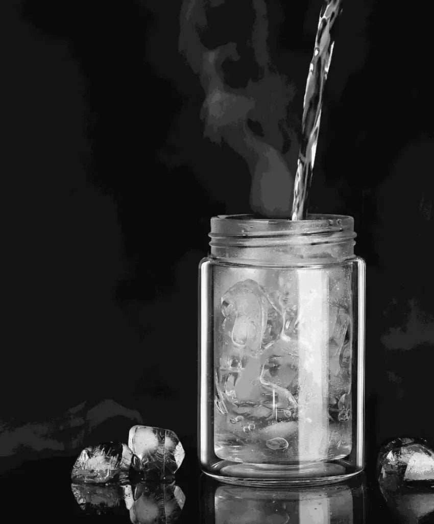 Glass jar with ice cubes and liquid being poured against a dark background