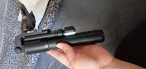 Hand holding a black selfie stick with a blurred background