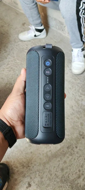 Person holding a black portable speaker on a concrete floor.