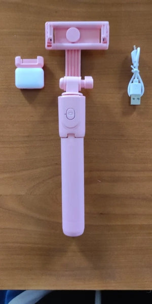 Pink smartphone selfie stick with accessories on a wooden surface