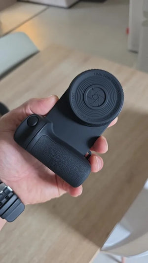 Hand holding a black camera lens on a light wooden surface